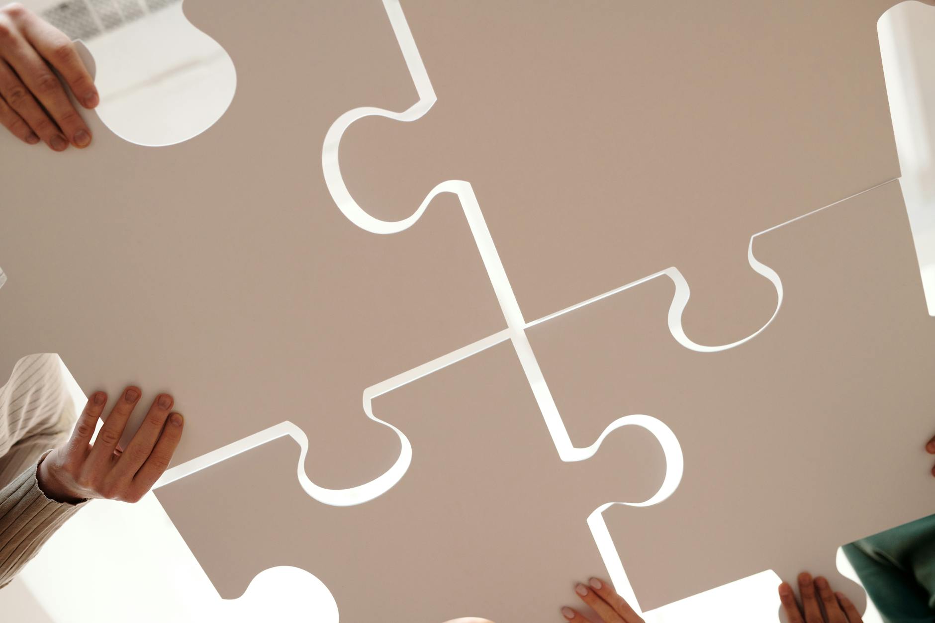 A low angle shot of hands holding paper cutouts of jigsaw puzzle pieces and helping to connect them